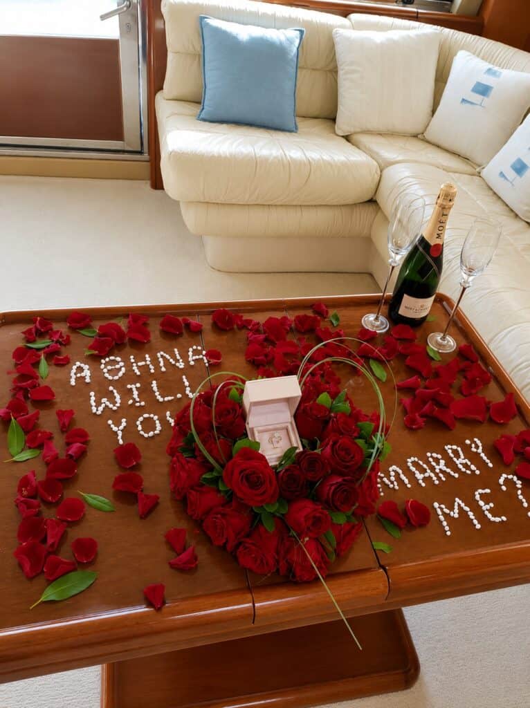 Valentine's Day romantic setup with roses, champagne, and message on table.
